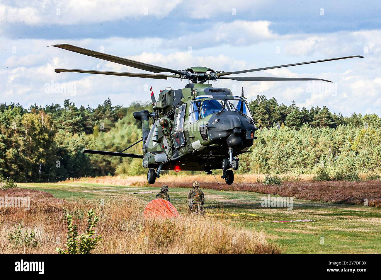 Länderübergreifende Großübung Eichkater 2024: Niedersachsen und Bayern üben gemeinsam die Bekämpfung von Vegetationsbränden Airbus Mehrzweckhubschrauber NH-90 der Bundeswehr vom Transporthubschrauberregiment 10 Lüneburger Heide des Fliegerhorstes Faßberg beim Feuerlöschhilfe-Einsatz, zwei Soldaten hängen die Halterung des leeren Bambi Bucket Löschwasserbehäters in den Lasthaken des NH-90 eaken. Der Pilot muss den etwa 7 Tonnen schweren NH-90 trotz Windböen mannshoch im Schwebeflug über dem Erdboden halten. Übungsgebiet Klosterforst Landkreis celle, Niedersachsen Germany *** major cross-state exe Foto Stock