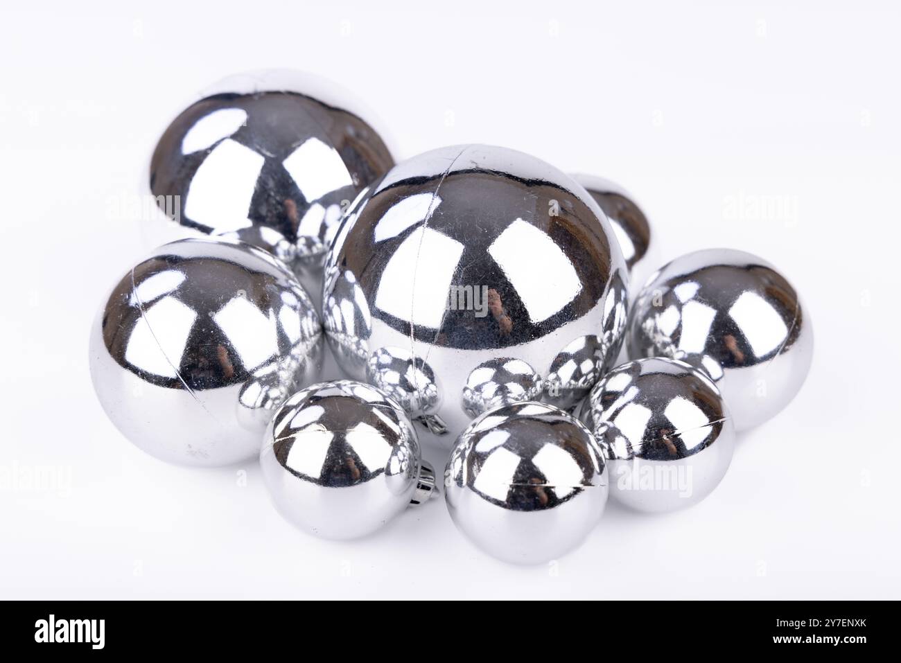 Un set di palline di Natale in argento lucido in varie misure posizionate su uno sfondo bianco, per creare una scena semplice e festosa per le festività natalizie Foto Stock