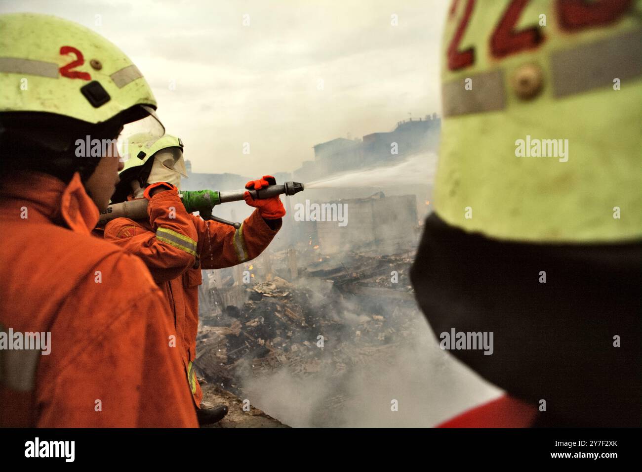 I vigili del fuoco che eseguivano la fase di raffreddamento dopo un incendio hanno bruciato centinaia di case in un quartiere denso di Jakarta, Indonesia. Foto Stock