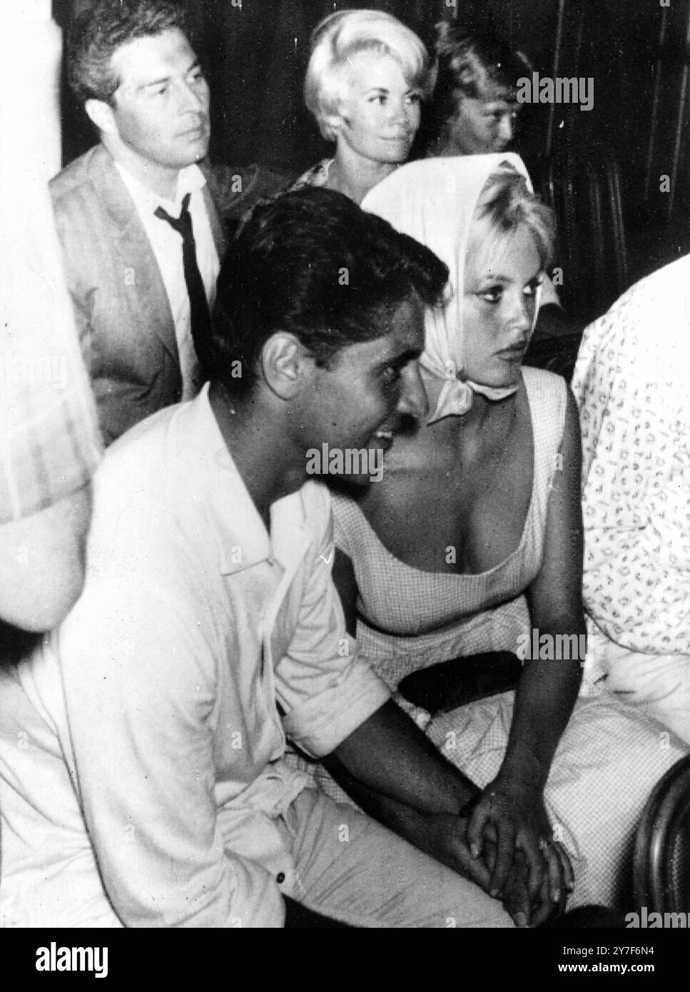 Star Studded Wedding on the Riviera la giovane star francese del cinema Brigitte Bardot ascolta attentamente durante il matrimonio della sua amica, l'attore Moustache. La sua escort con la quale batte le mani è il chitarrista Sacha Distel. Tra le altre personalità al matrimonio vi sono il figlio di Charlie Chaplin, Sidney, seduto dalla ballerina/attrice francese Noelle Adam (in background). Juan Les Pins, 13 agosto 1958 Foto Stock