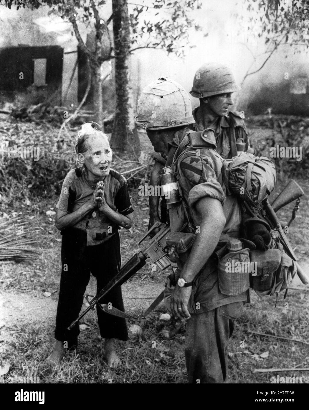 Con il suo villaggio che brucia alle sue spalle, un'anziana donna vietnamita supplica un soldato della 1st Cavalry Division americana, mentre un plotone di ricognizione esplorava un'area vicino a Bong Son, a circa 300 miglia a nord-est di Saigon.19 maggio 1966. Foto Stock