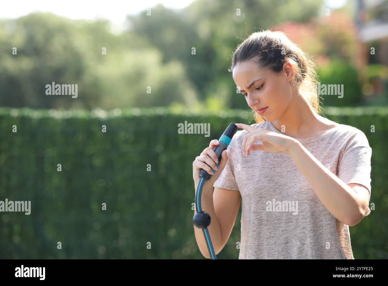 Donna che controlla l'ugello bloccato di un tubo in giardino Foto Stock