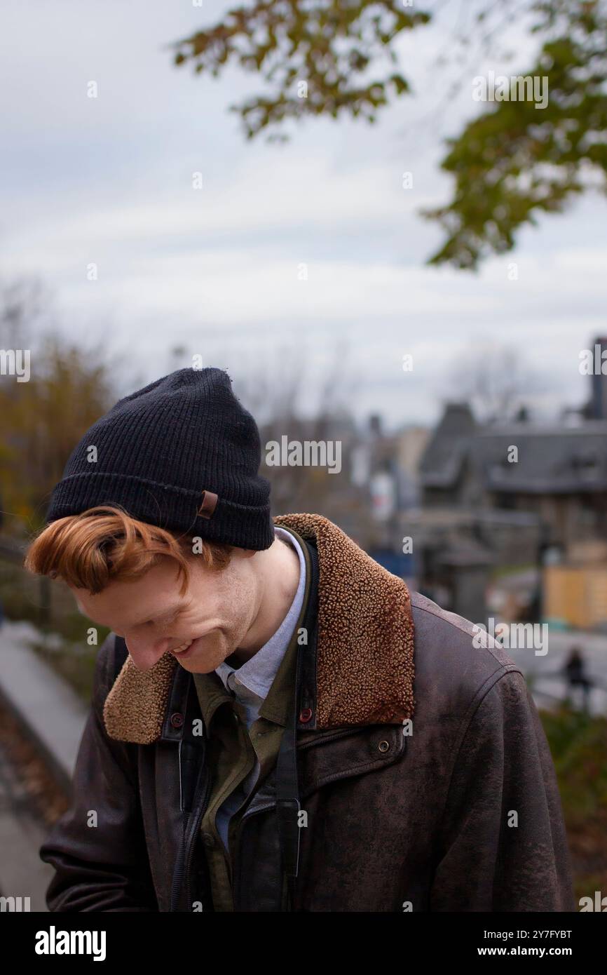 Un uomo con i capelli rossi e un berretto sorride in un parco in un giorno d'autunno Foto Stock