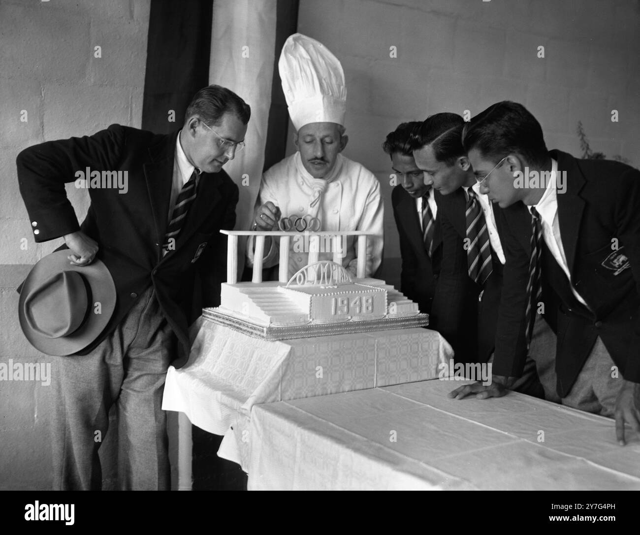 Lo Chef Olimpico presenta la torta 'Greek Theatre' allo Sri Lanka (allora conosciuto come Ceylon) i rappresentanti olimpici quando i membri della squadra olimpica dello Sri Lanken si sono trasferiti nel Villaggio Olimpico di Richmond , Surrey , oggi il signor John Weider, chef olimpico di cucina del campo, ha presentato loro una torta fatta in forma di teatro greco. Non appena tutti i concorrenti di Srik Lanken arriveranno, la torta sarà tagliata. Lo chef e i membri olimpici dello Sri Lanken ammirano oggi la torta Olympiad 1948 a Richmond , Surrey . Da sinistra a destra , Brant Little ( Sri Lanka Team Coach ) , John Weider ( Olympic Foto Stock