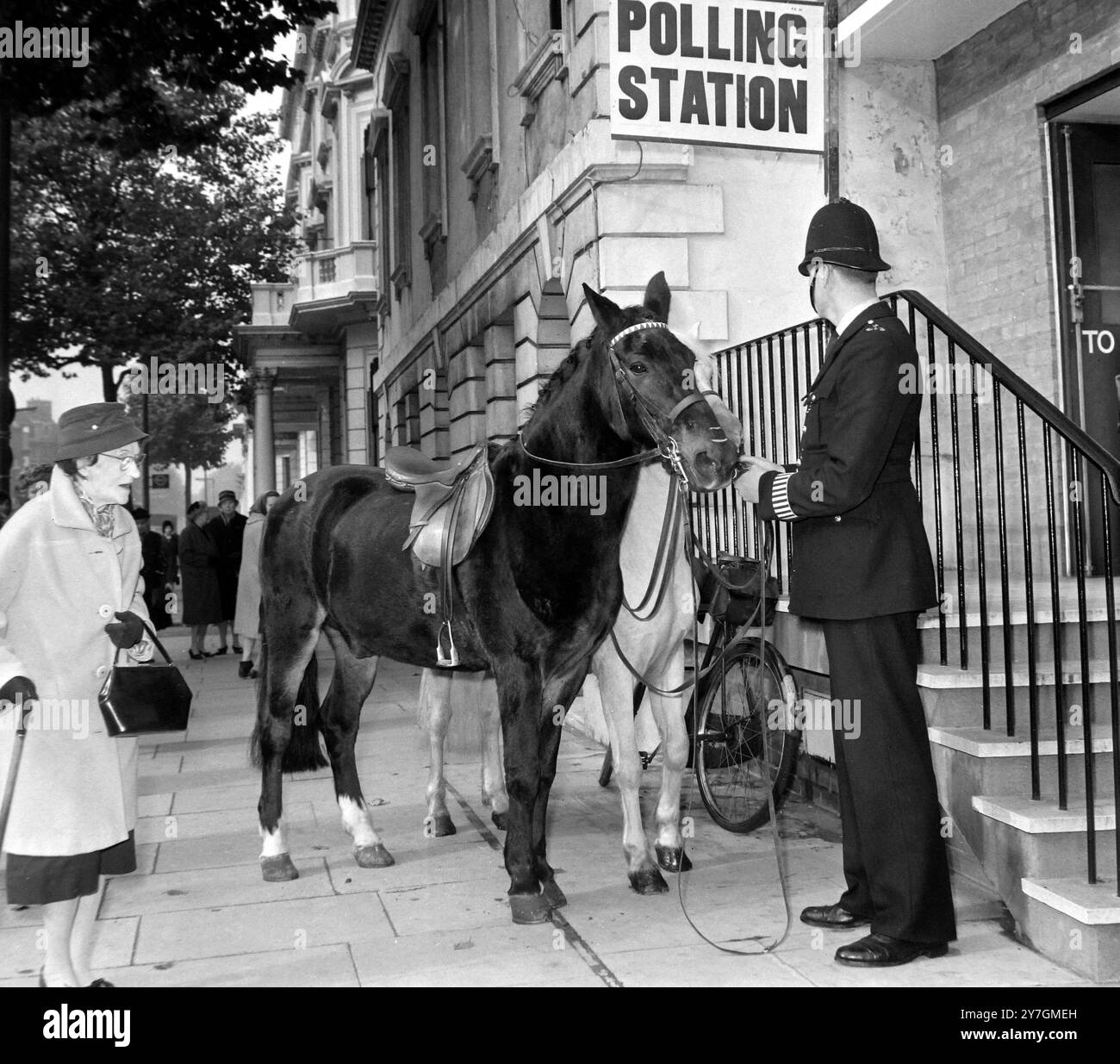 15 OTTOBRE 1964 Un poliziotto tiene un cavallo mentre il suo cavaliere vota all'interno del seggio elettorale locale durante le elezioni generali. Knightsbridge, Londra, Inghilterra. Foto Stock