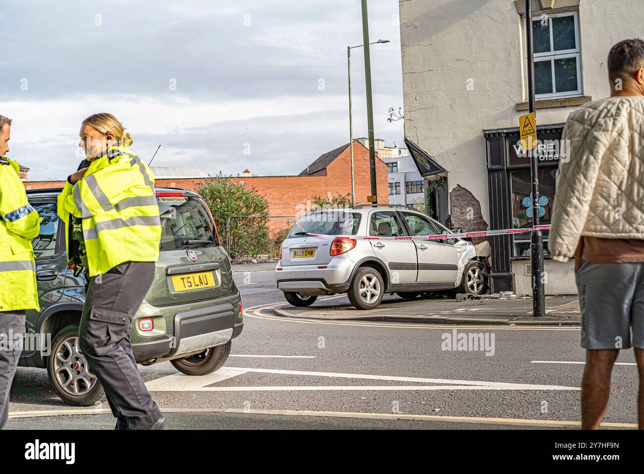 Vista laterale di una piccola auto che si è schiantata all'ingresso di un negozio di fiori, l'auto è circondata da un nastro adesivo, fuoco non incrociare. Agenti di polizia Foto Stock