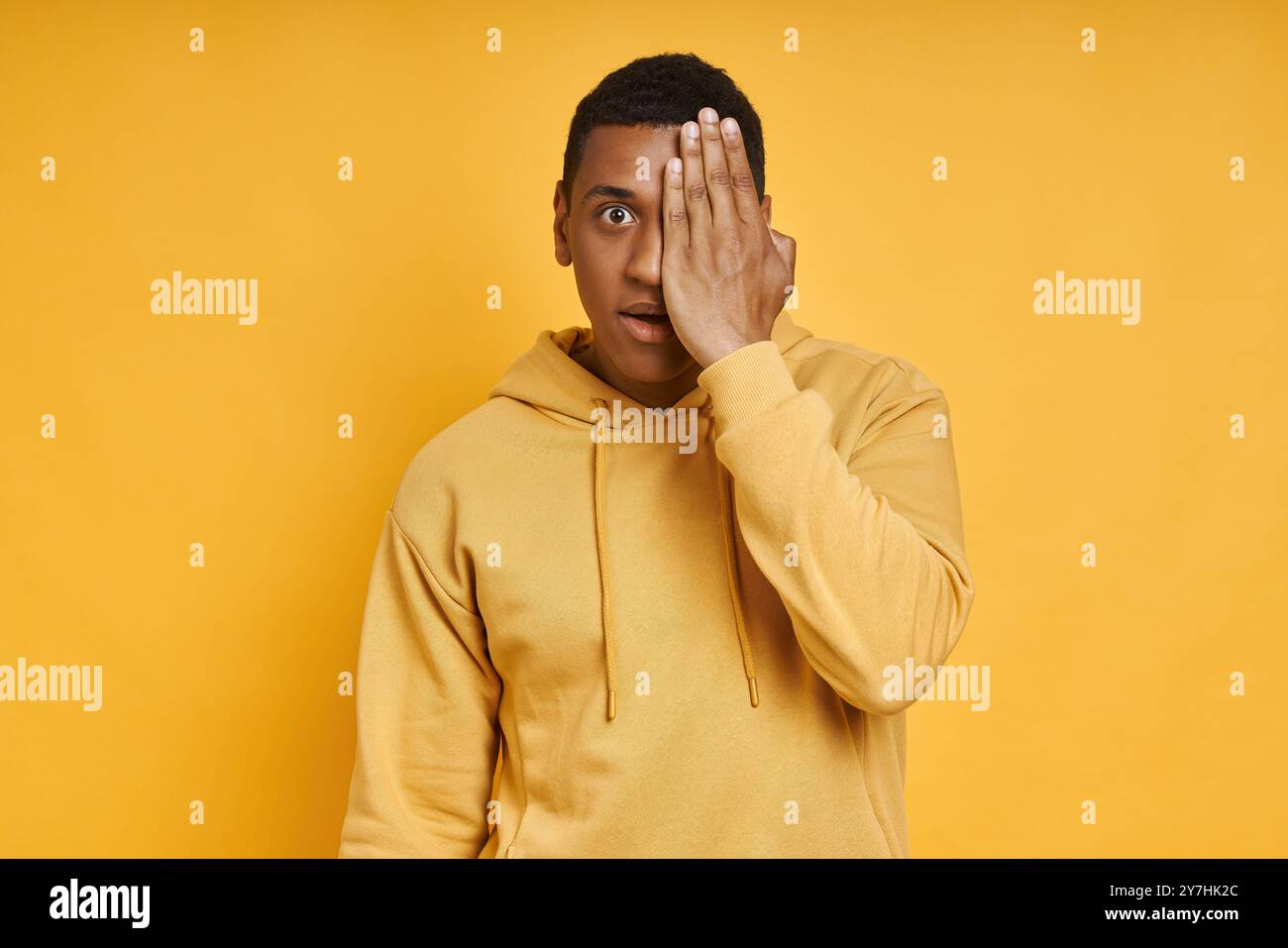 Scioccato uomo da corsa misto che copre mezza faccia con la mano mentre è in piedi su sfondo giallo Foto Stock Scioccato uomo da corsa misto che copre mezza faccia con la mano mentre è in piedi su sfondo giallo Foto Stock