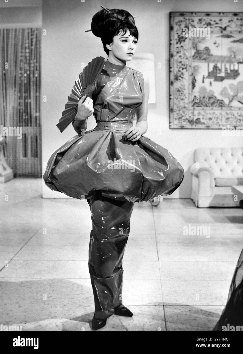 13 MAGGIO 1964 bellezza strisciante. Guardando un po' da sogno, Shirley MacLaine, dov'è la creazione unica di Edith Head in una scena di "What a Way to Go". L'abito è probabilmente l'unico costume in pelle verniciata al mondo. Doveva essere assemblato con cemento liquido, proprio sulla stella. La gonna estremamente sottile è così stretta che richiede una passeggiata scorrevole per poterla muovere. Realizzato nel rosso cinese più brillante, l'abito è un nuovo pouff di funghi se prugna ai fianchi. Hollywood, California, Stati Uniti Foto Stock