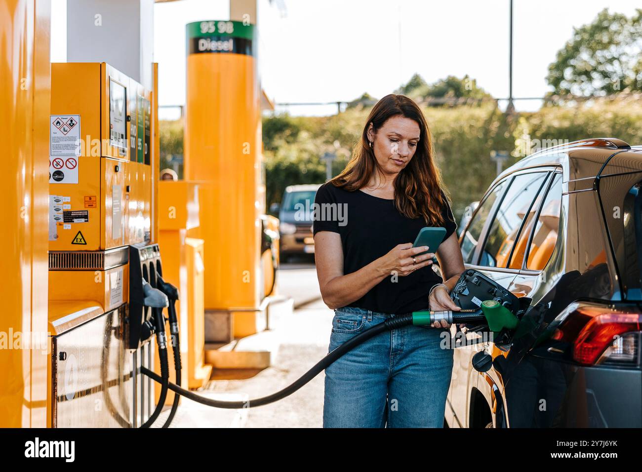 Donna che usa lo smartphone mentre rifornisce l'auto al distributore di benzina Foto Stock