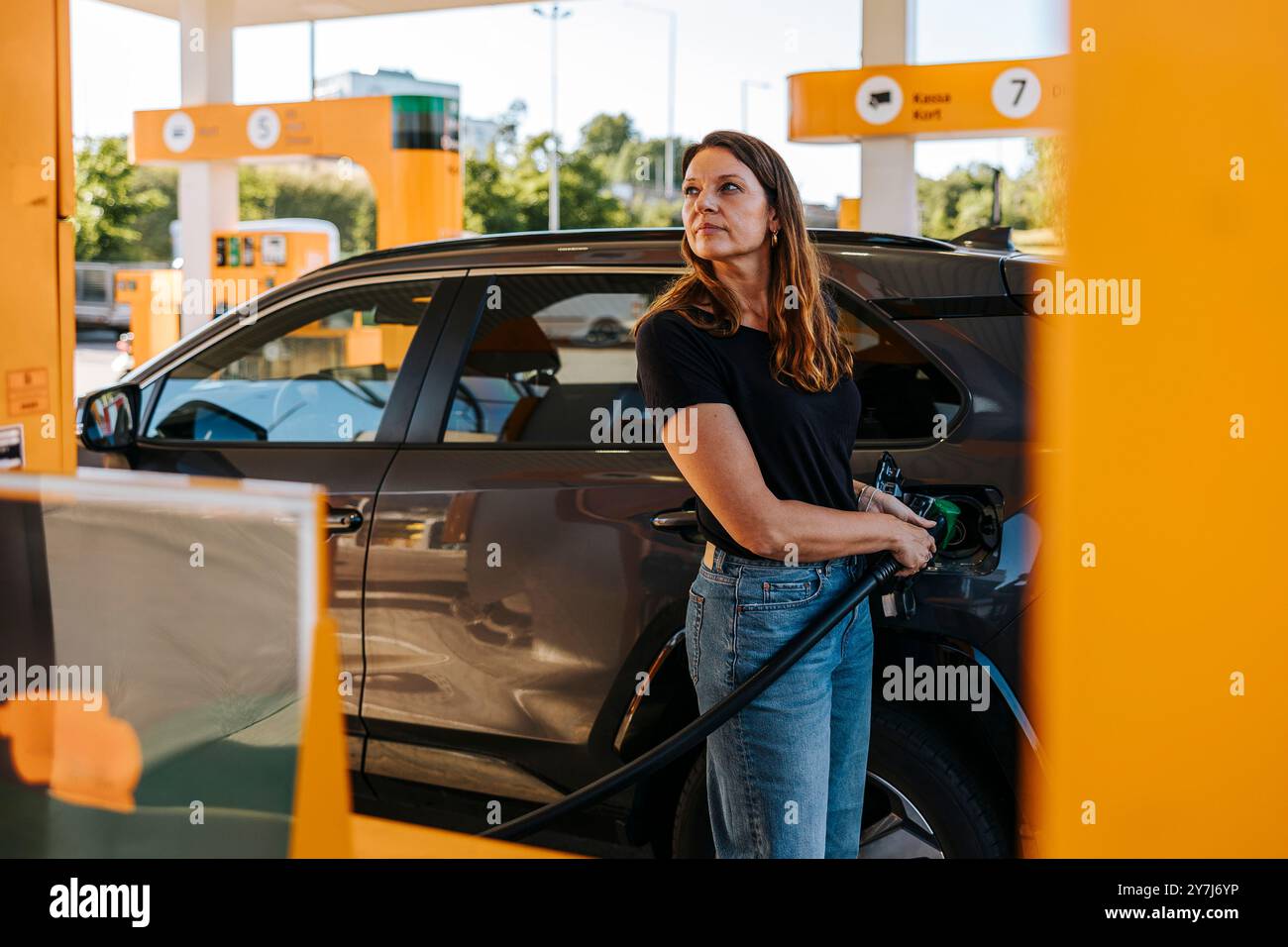 Donna matura che guarda lontano mentre fa rifornimento di auto alla pompa di carburante Foto Stock