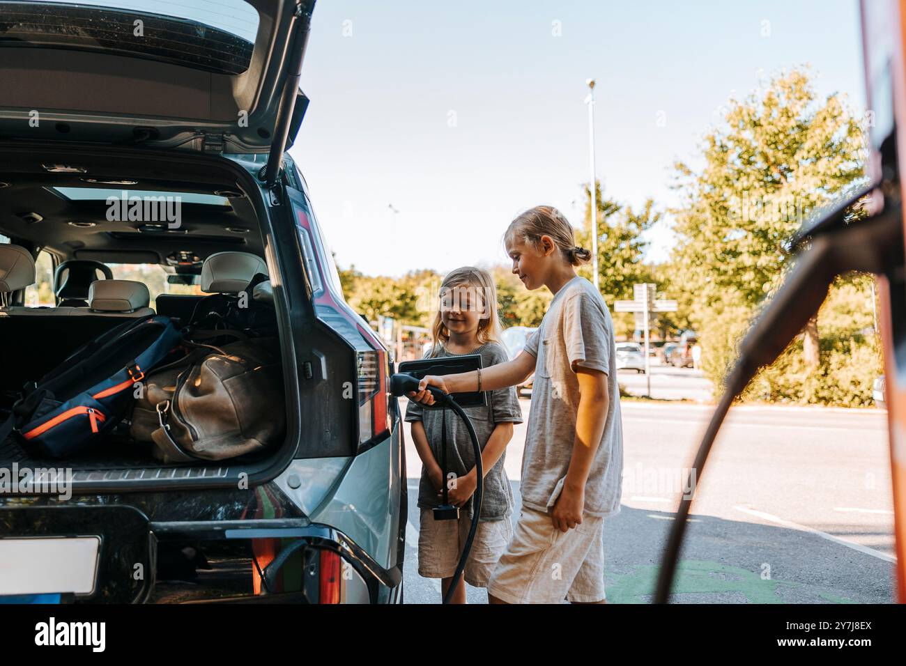 Fratello che carica l'auto elettrica mentre è in piedi alla stazione Foto Stock