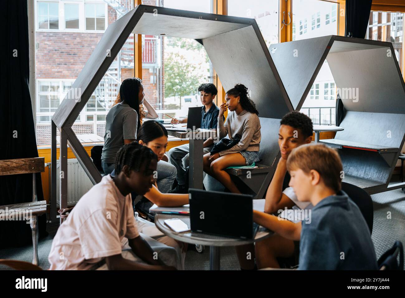 Gruppo di studenti maschi e femmine che studiano insieme attraverso un computer portatile mentre si siede in una caffetteria a scuola Foto Stock