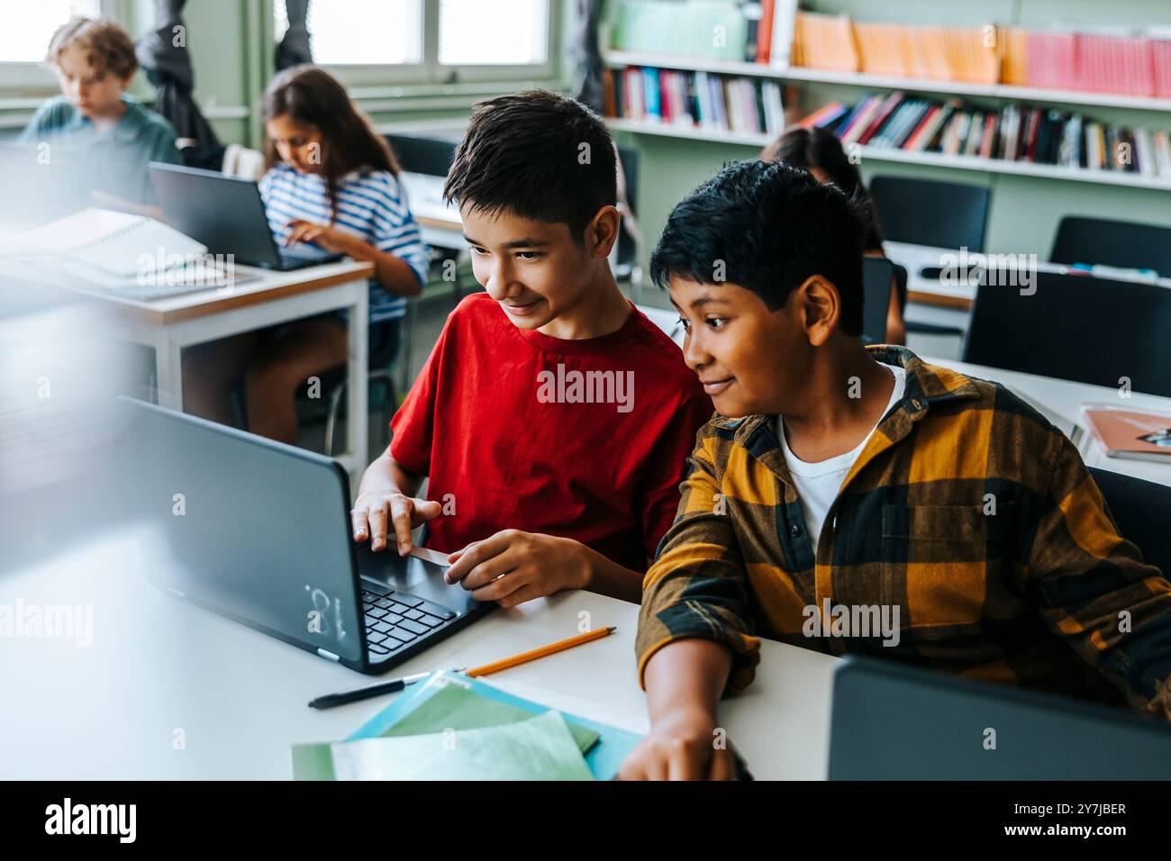 Vista ad angolo alto del ragazzo che studia con un compagno di classe su un computer portatile mentre è seduto in classe alla scuola elementare Foto Stock