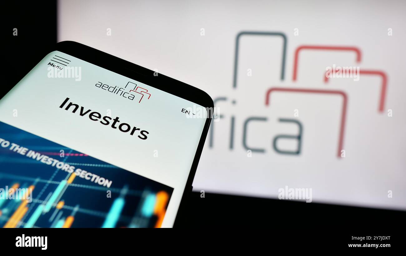 Telefono cellulare con sito web della società immobiliare belga Aedifica SA sullo schermo davanti al logo aziendale. Mettere a fuoco in alto a sinistra sul display del telefono. Foto Stock