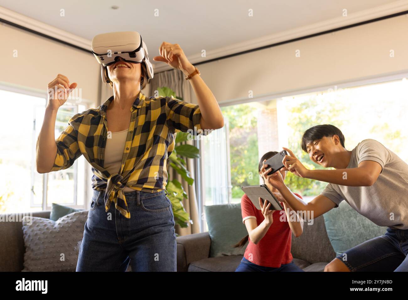 Utilizzando il visore VR, la madre si diverte a giocare in realtà virtuale con la famiglia a casa Foto Stock