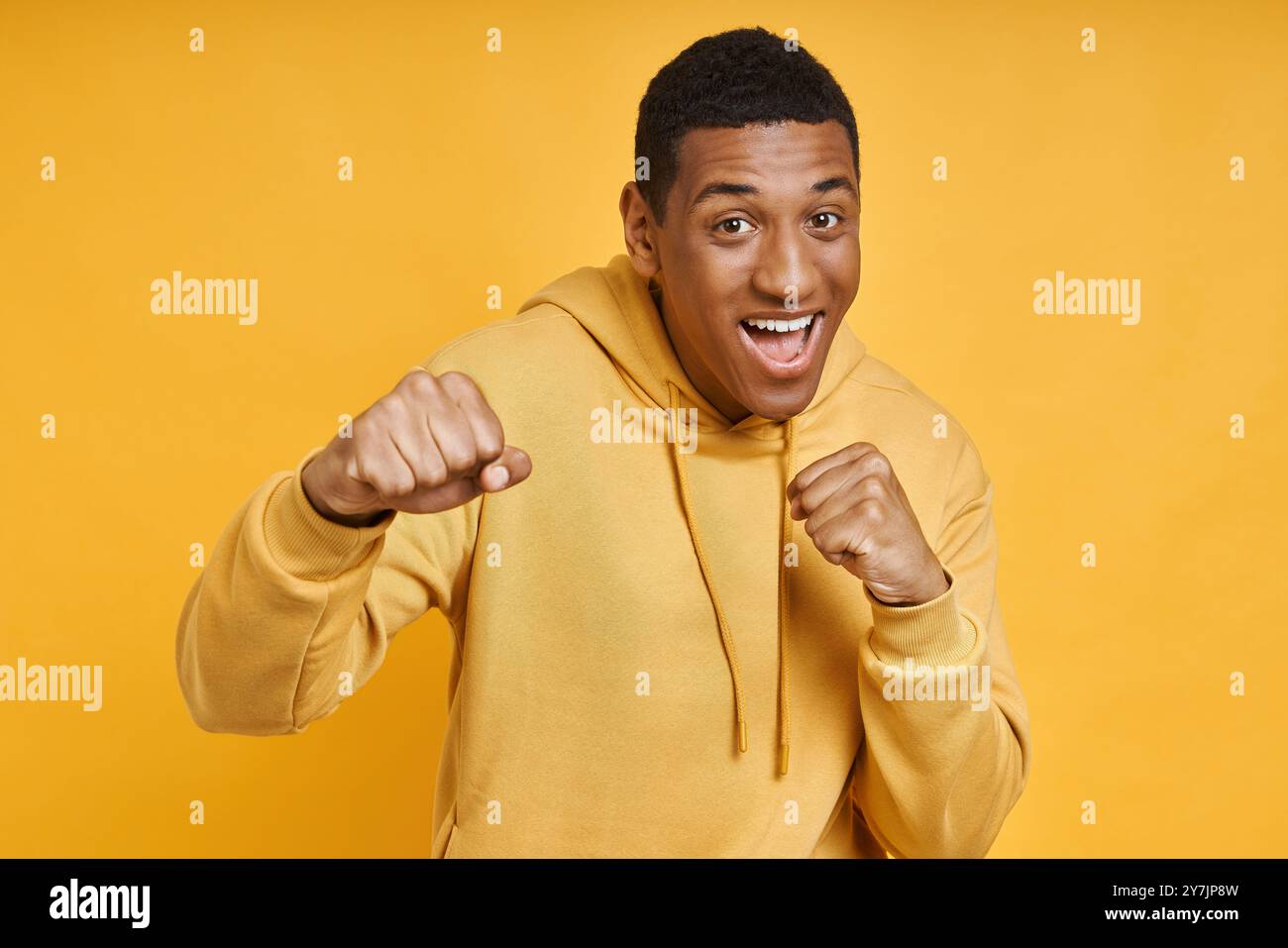 Giocoso uomo di razza mista in posa con un pugno su sfondo giallo Foto Stock