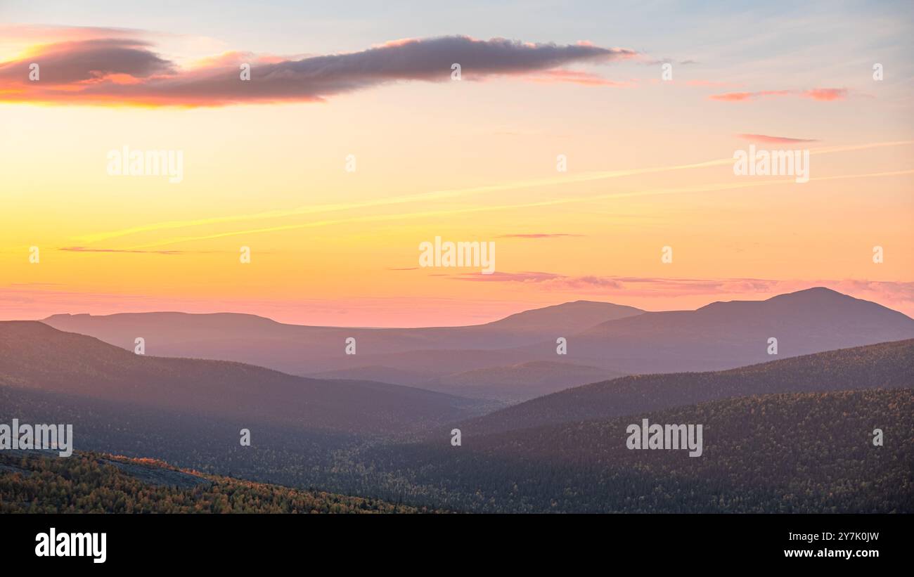 Tranquillo paesaggio montano al tramonto, che mostra colline ondulate sotto un cielo pastello con sfumature arancio e rosa. Foto Stock