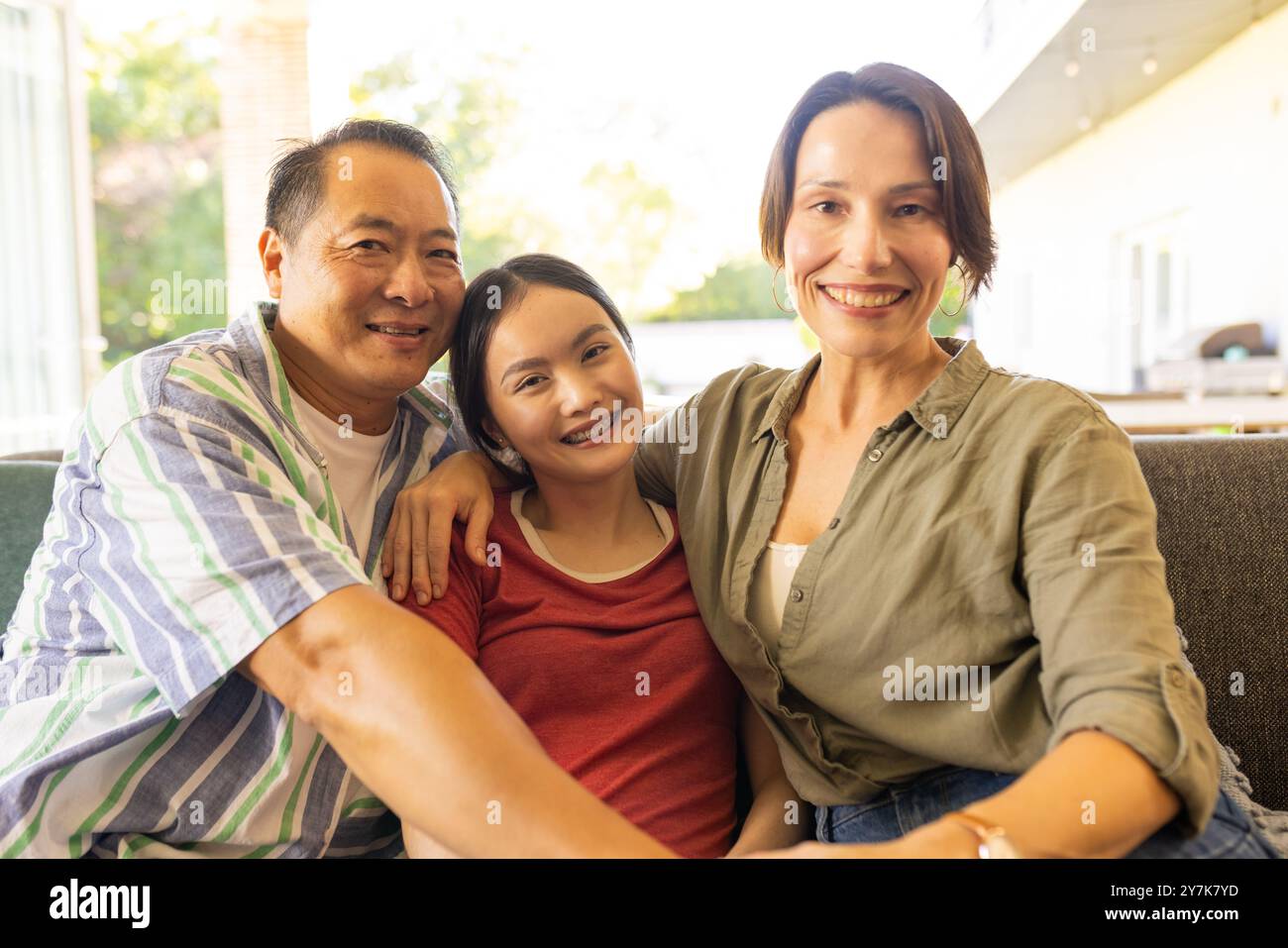 Una famiglia sorridente di tre persone sedute insieme sul divano, godendosi del tempo di qualità Foto Stock