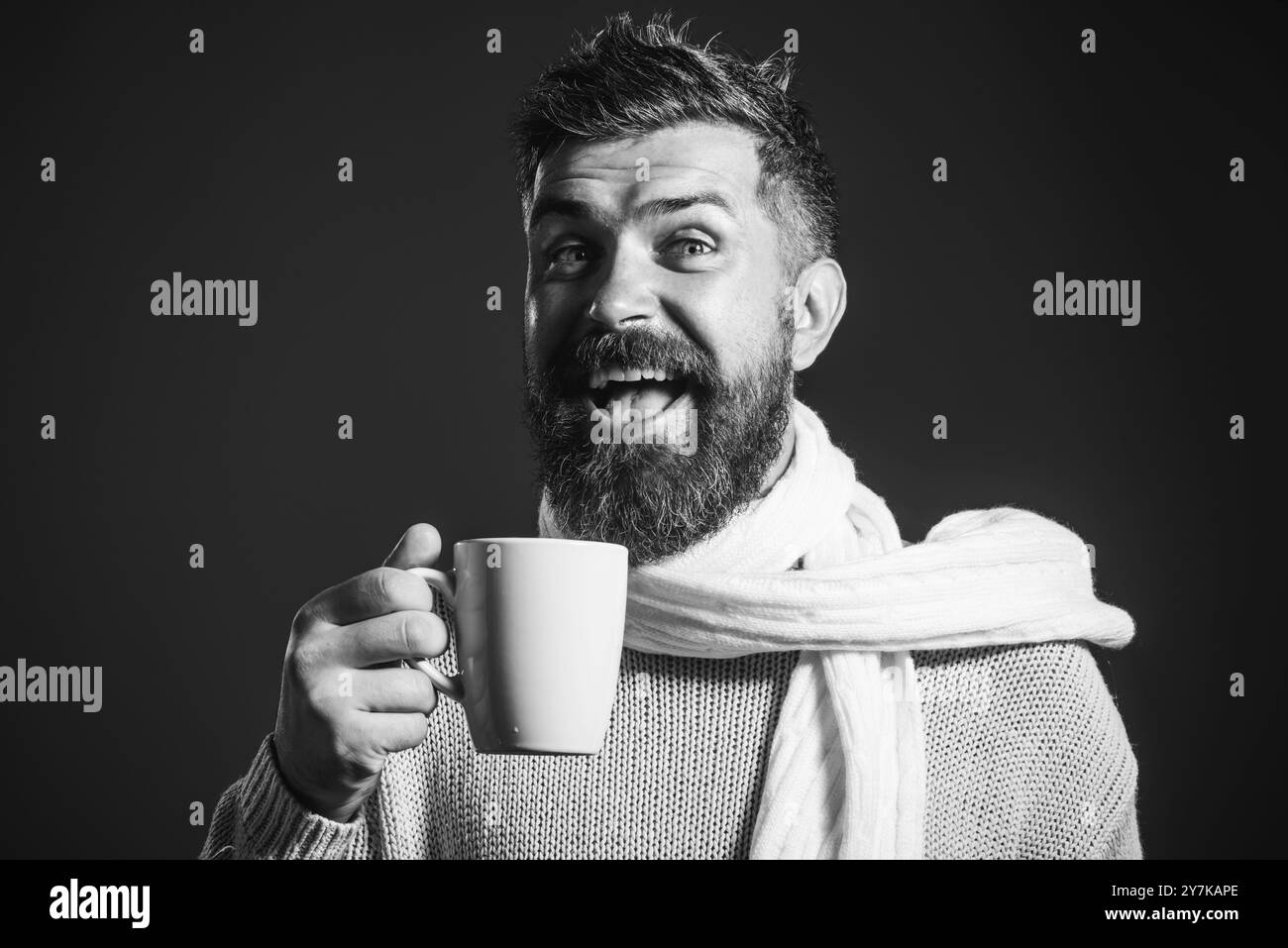 Uomo barbuto felice in maglione e sciarpa con tazza di caffè o tè. Bell'uomo con barba e baffi che si gusta una tazza di caffè o un cappuccino nel caffè. S Foto Stock