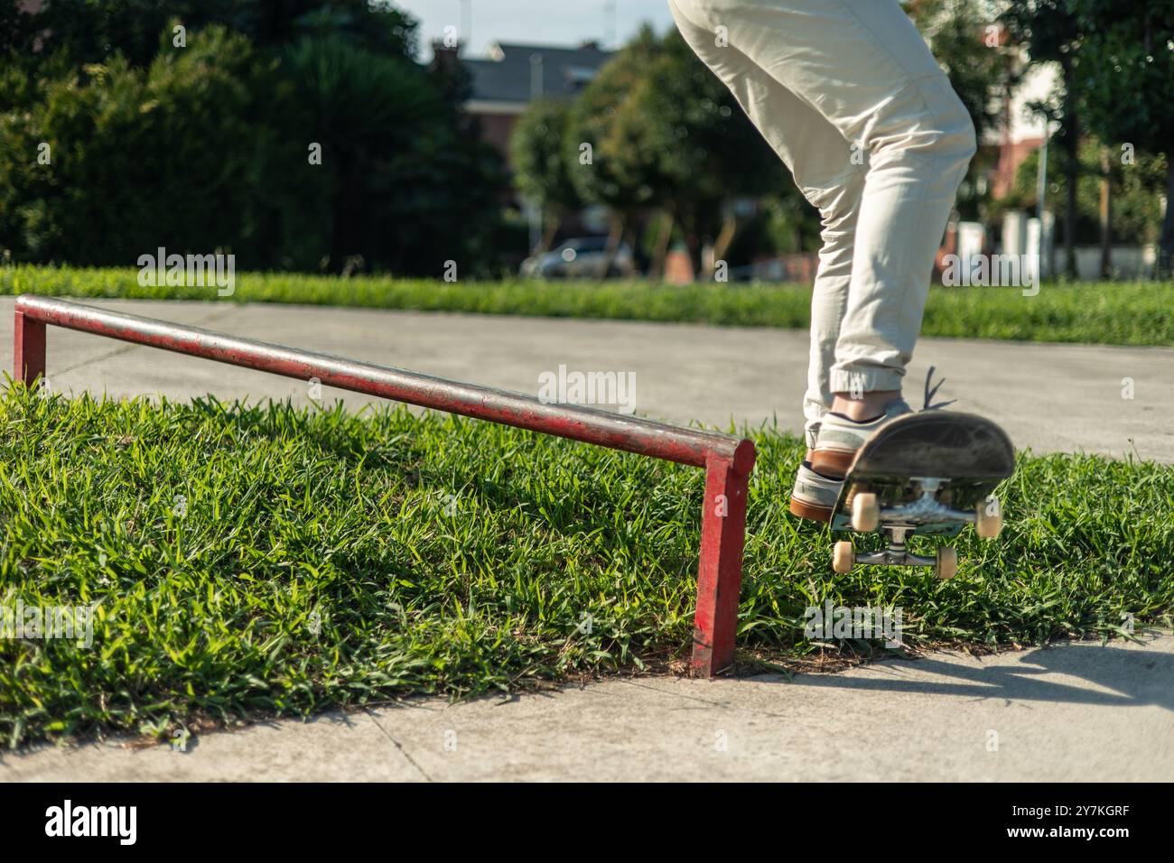 avvicinati alle gambe di uno skater mentre completano una macinatura su un vivace binario rosso nello skate park. L'attenzione rivolta alla parte inferiore del corpo dello skater mette in risalto la te Foto Stock