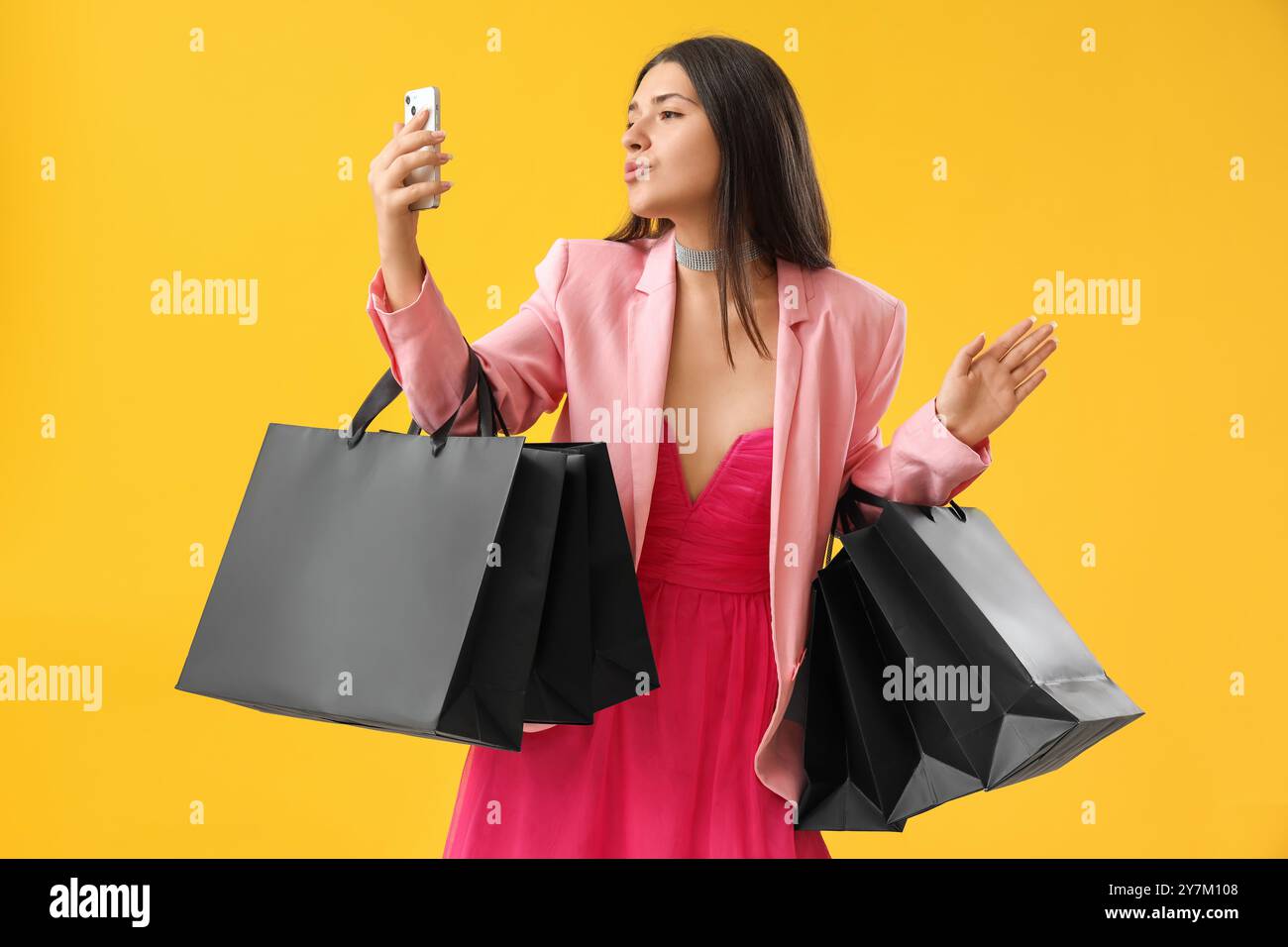 Giovane donna con borse della spesa e cellulare su sfondo giallo. Promozione Black Friday Foto Stock