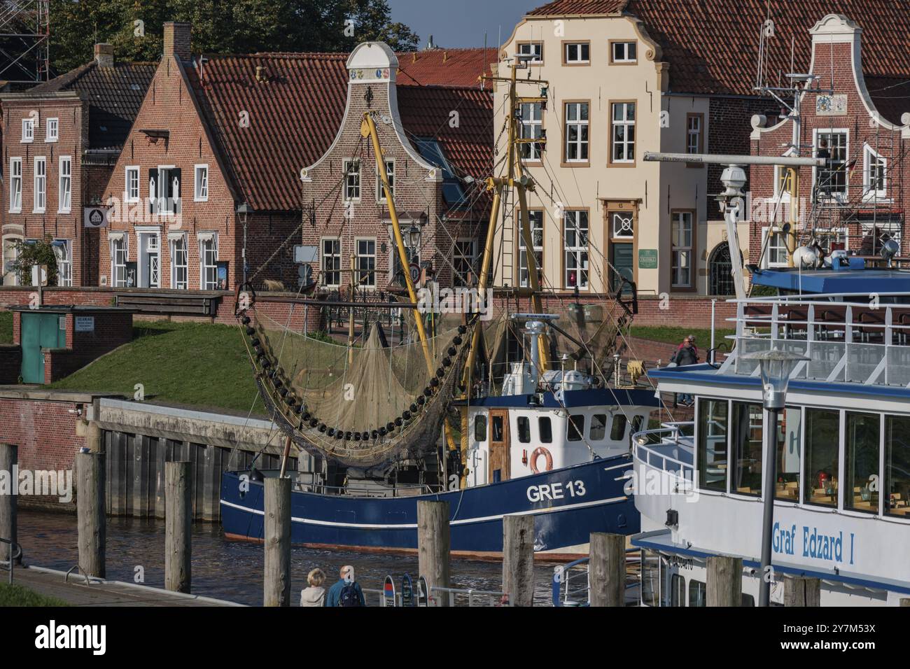 Una barca da pesca su una banchina di fronte a affascinanti case storiche e un cielo azzurro, greetsiel, mare del nord, germania Foto Stock