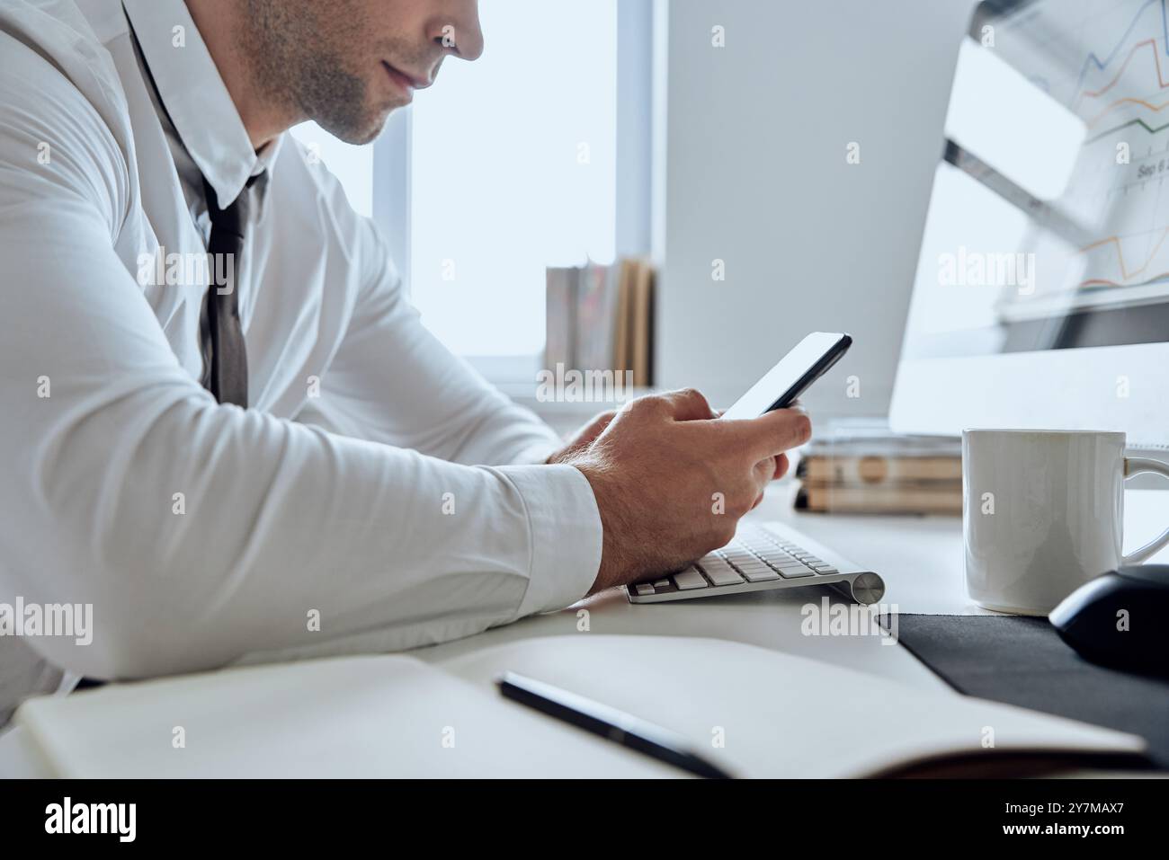 Primo piano di un uomo in camicia e cravatta con uno smartphone mentre è seduto sul posto di lavoro in ufficio Foto Stock