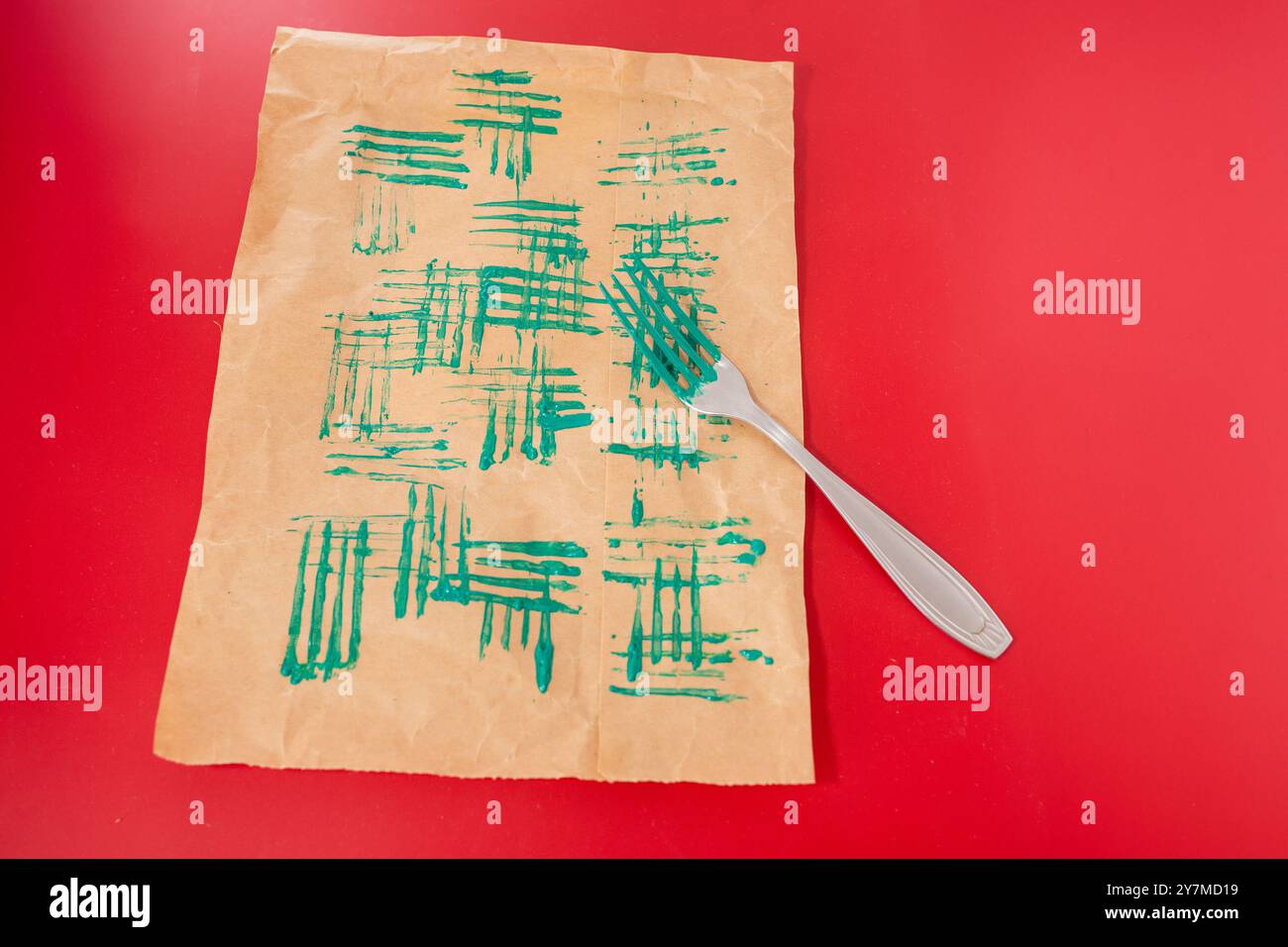 un foglio di carta marrone con motivi di vernice verde creato dai denti di una forchetta, vista dall'alto, sfondo rosso Foto Stock