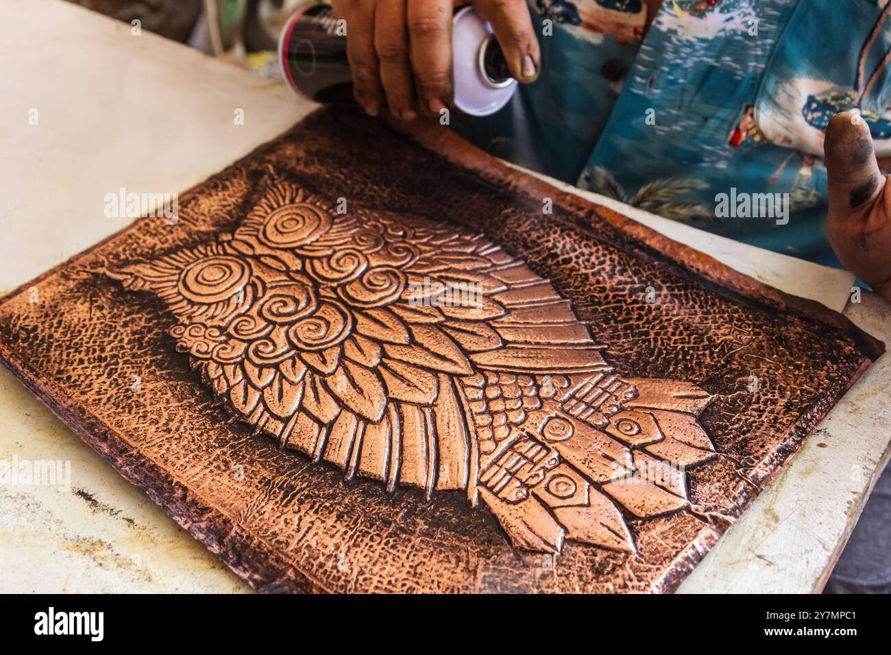 Primo piano di un artigiano che applica la vernice su un foglio di rame inciso con un dettagliato motivo a gufo, utilizzando una tecnica di invecchiamento per preservare l'annata, Weathe Foto Stock