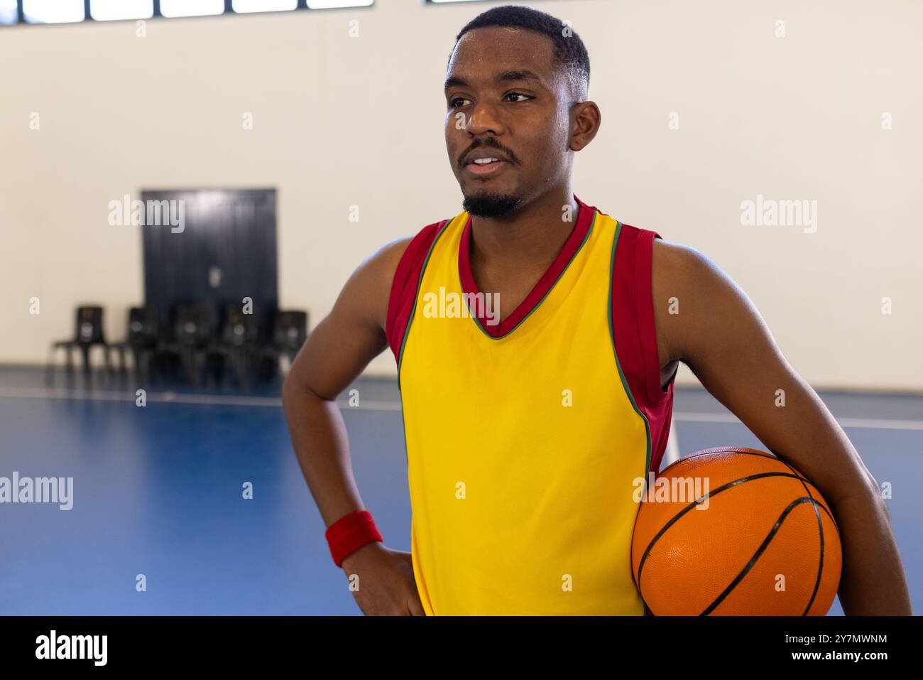 Con il pallacanestro, l'uomo in maglia sportiva in piedi sul campo al coperto, sembra concentrato Foto Stock