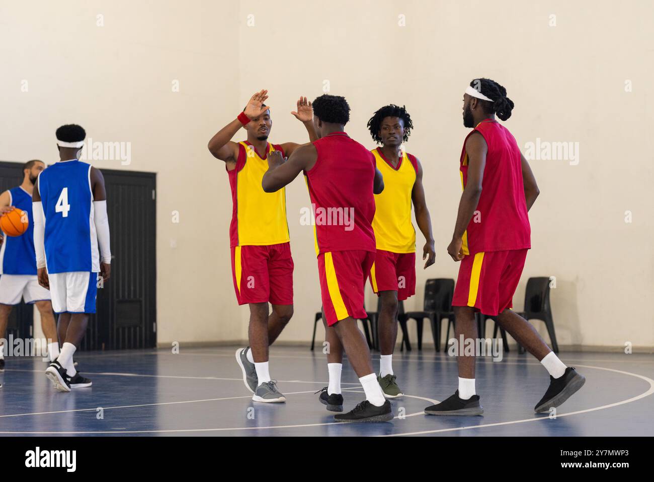 Giocare a basket nella palestra scolastica, fare squadra per festeggiare il successo, indossare uniformi Foto Stock