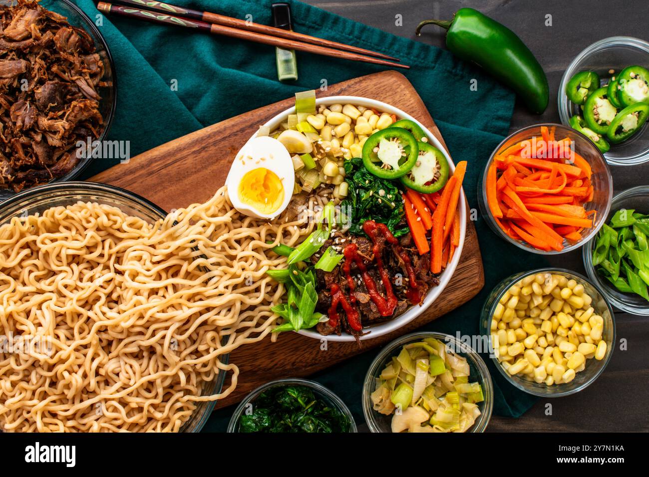 Tagliatelle Ramen versate in una ciotola di maiale e verdure Ramen: Ramen condito con un uovo sodo, peperoni caldi, carote, scalpelli e spinaci Foto Stock