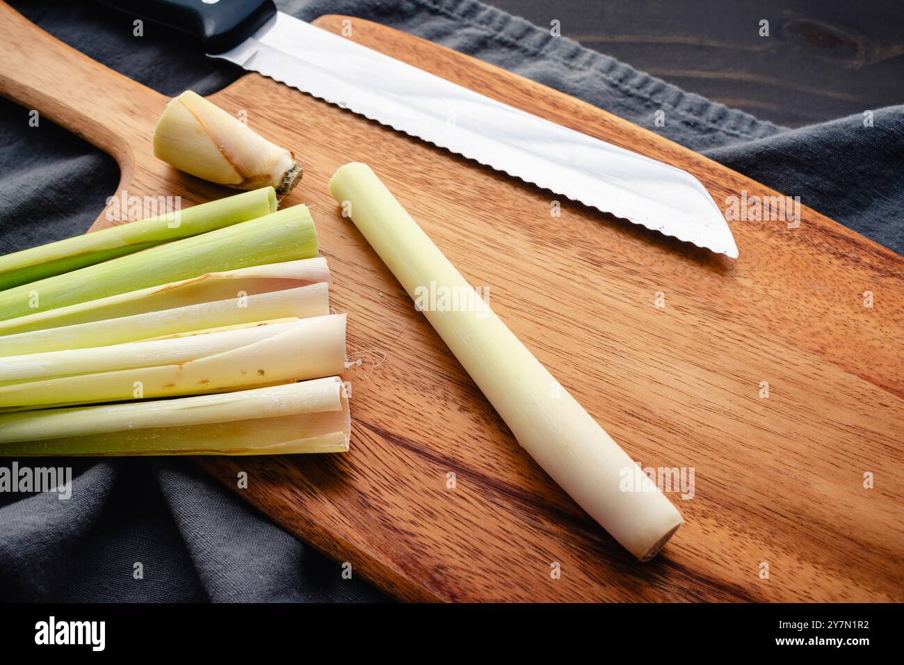 Primo piano di uno stelo di citronella tagliato e sbucciato: Tagliare e pelare uno stelo di citronella su un tagliere di legno con un coltello seghettato Foto Stock