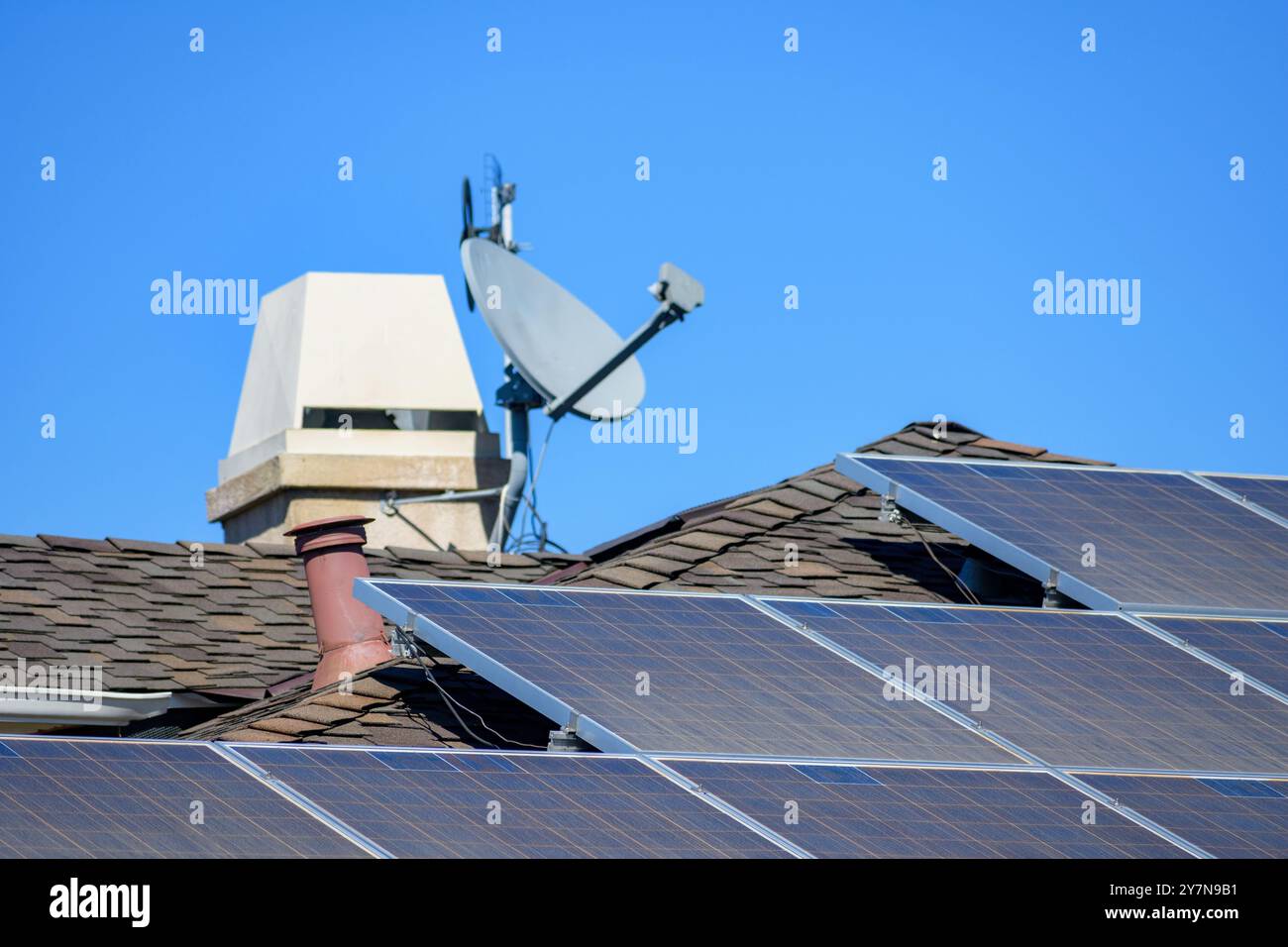 Pannelli solari installati su un tetto martellato marrone con camino sfocato e parabola satellitare sullo sfondo. Messa a fuoco selettiva Foto Stock