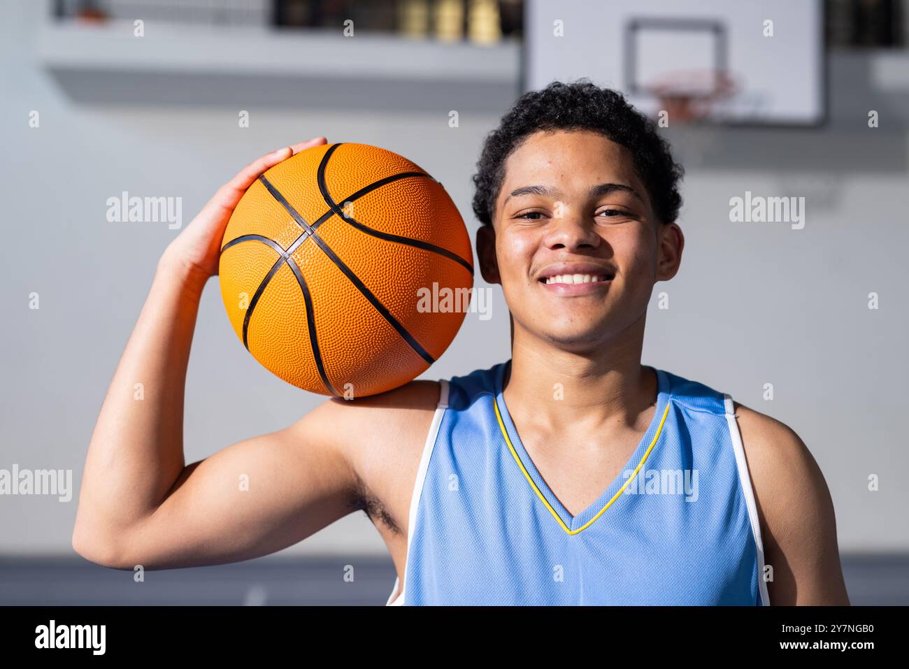 Ragazzo sorridente che tiene il basket in palestra, pronto per la partita e per praticare sport Foto Stock
