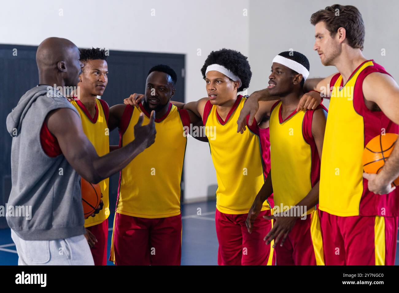 Allenatore di pallacanestro che parla con la squadra, i giocatori ascoltano e tengono in mano palle da basket Foto Stock