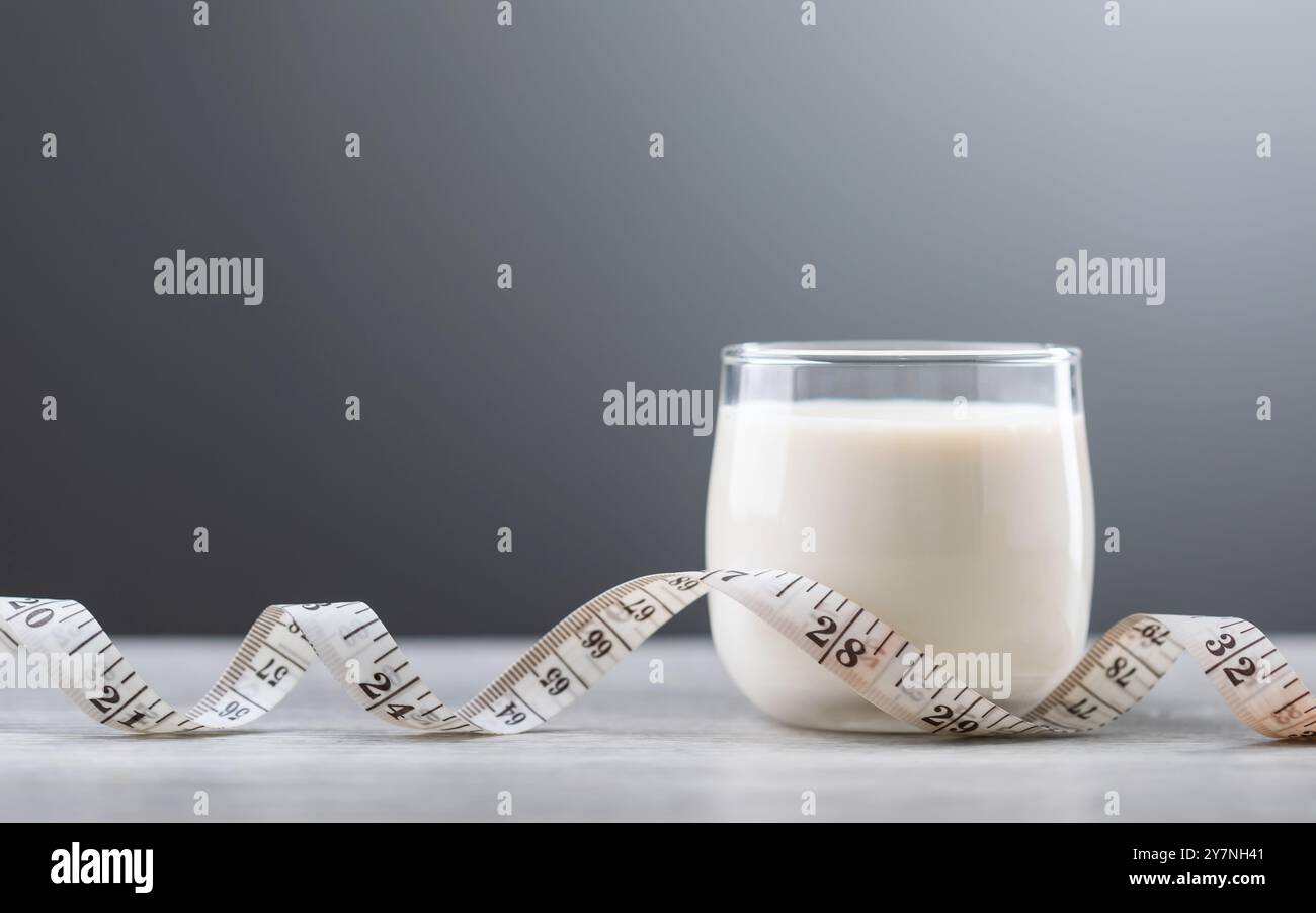 Un bicchiere di latte e un metro a nastro sul tavolo. Concetto di incorporare il latte in una dieta sana e un programma di fitness, evidenziandone il bene nutrizionale Foto Stock