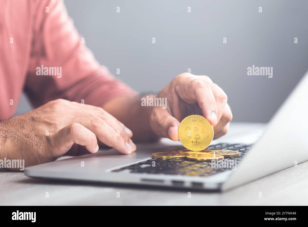 Man possiede un Bitcoin d'oro mentre utilizza un laptop, che rappresenta Bitcoin come una forma di valuta digitale per le transazioni online, evidenziando il concetto Foto Stock