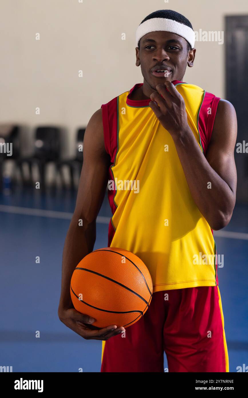 In possesso di pallacanestro, giocatore in uniforme sportiva in piedi su un campo coperto Foto Stock