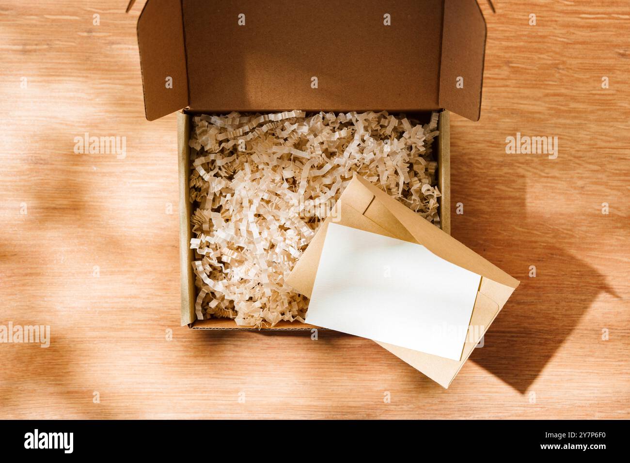 Scatola di cartone aperta riempita di carta triturata e un cartoncino vuoto su una superficie di legno Foto Stock