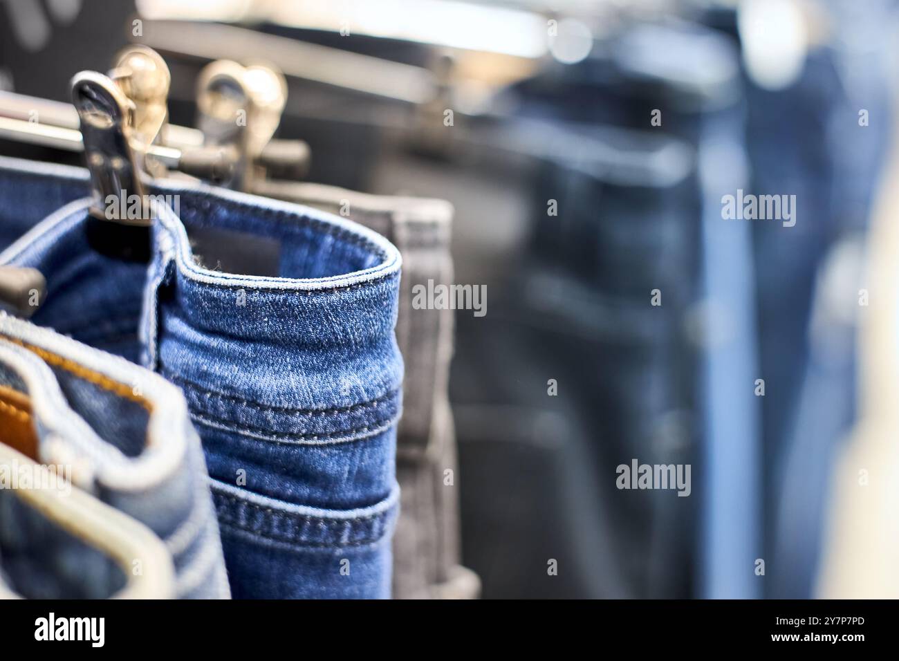 Jeans o pantaloni in denim appesi a un gancio nel centro commerciale. Collezione di articoli di moda in negozio di abbigliamento in vendita. Industria tessile. Grigio blu e b Foto Stock