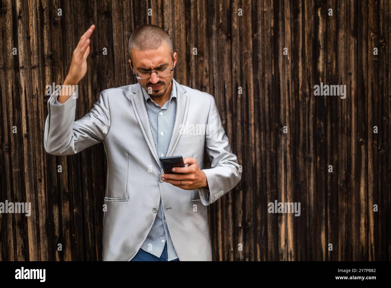 Ritratto di un uomo d'affari frustrato che invia messaggi al telefono. Sfondo in legno. Foto Stock