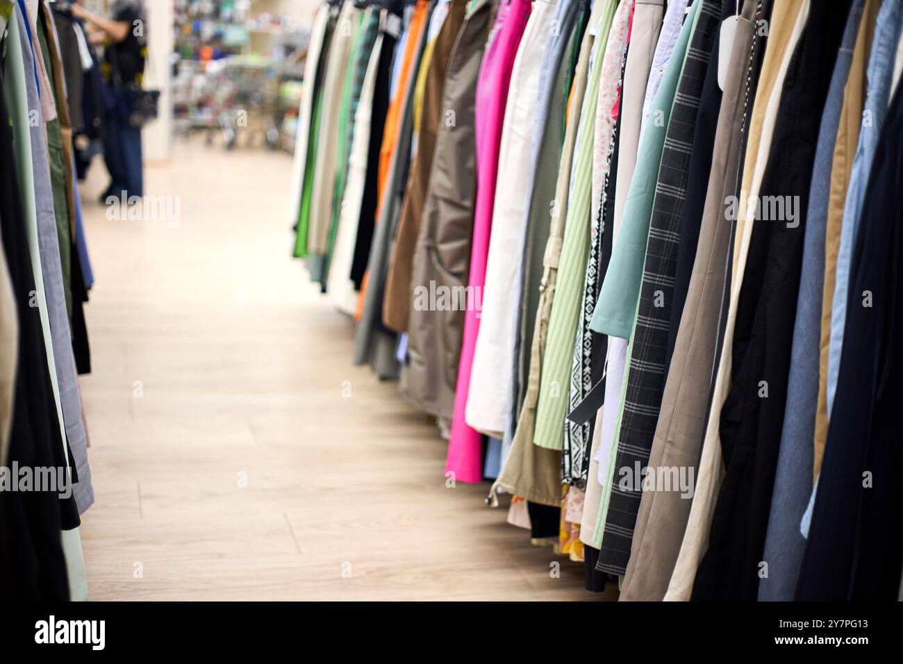 L'acquirente femminile fuori dal centro passa davanti ai negozi di abbigliamento femminile e ai rack di fila di negozi di abbigliamento. Centro commerciale con tantissimi abiti pantaloni abiti mirati. Foto Stock