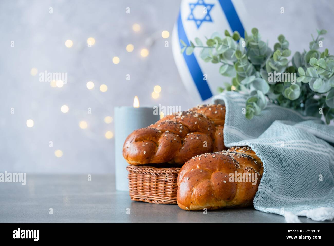 Challah fatta in casa, tradizionale pane intrecciato, candela, vino, Torah, bandiera di Israele sullo sfondo delle luci. Foto Stock