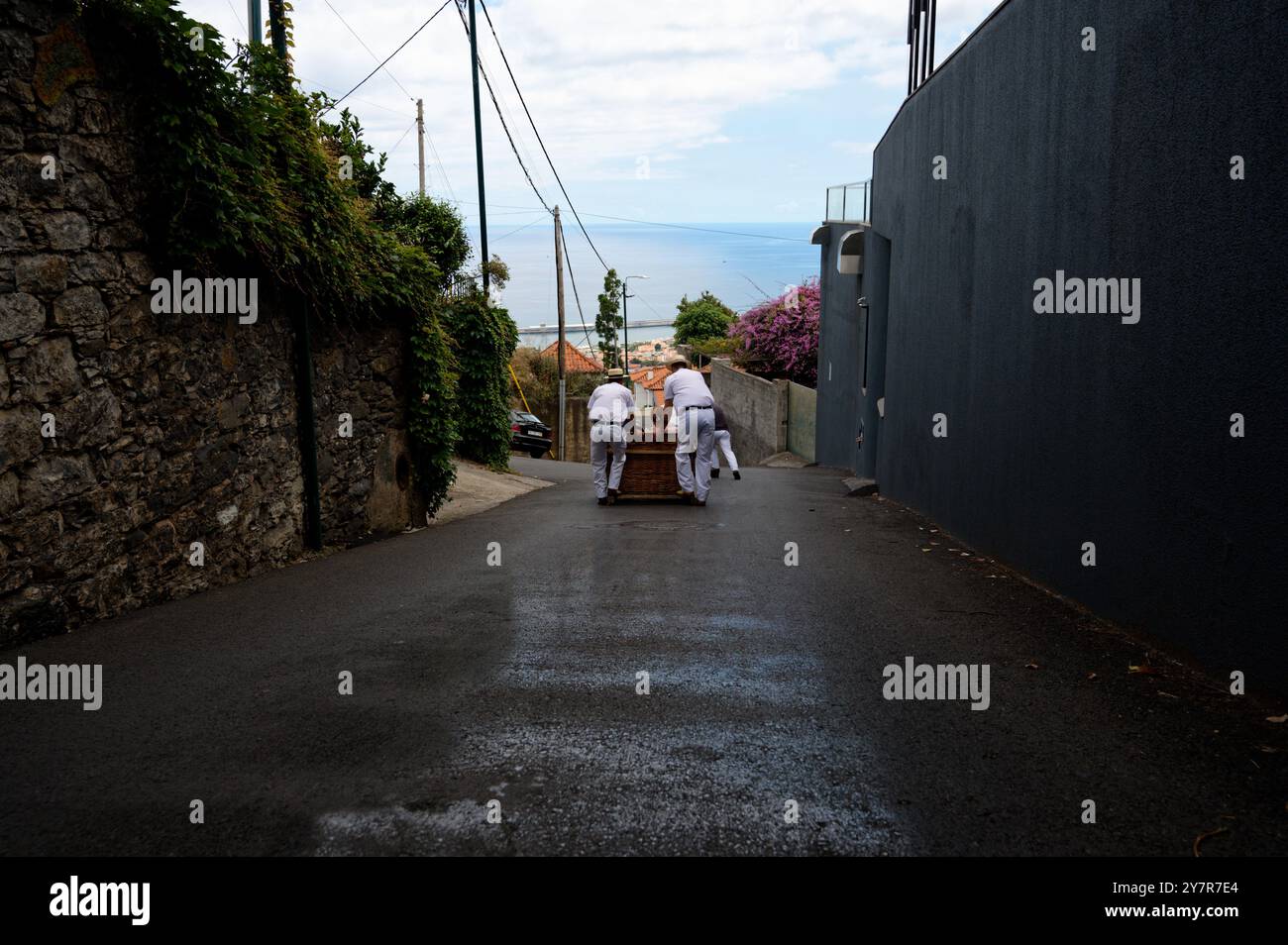 Carreiros guida un toboga in vimini lungo un vicolo cerato con vedute dell'oceano incorniciate da pietre e pareti moderne Foto Stock