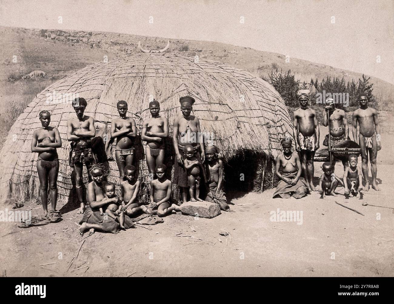 Fotografia d'epoca di nativi e kraal. Africani di fronte a una tradizionale capanna kraal. Sudafrica, tra il 1800 e il 1899. Kraal (anche scritto craal o kraul) è una parola afrikaans e olandese, usata anche nell'inglese sudafricano, per un recinto per il bestiame o altro bestiame, situato all'interno di un insediamento o villaggio dell'Africa meridionale circondato da una recinzione di rami spinosi, una palizzata, un muro di fango o altre recinzioni, grosso modo circolari. È simile a un bombardamento nell'Africa orientale o centrale. Foto Stock