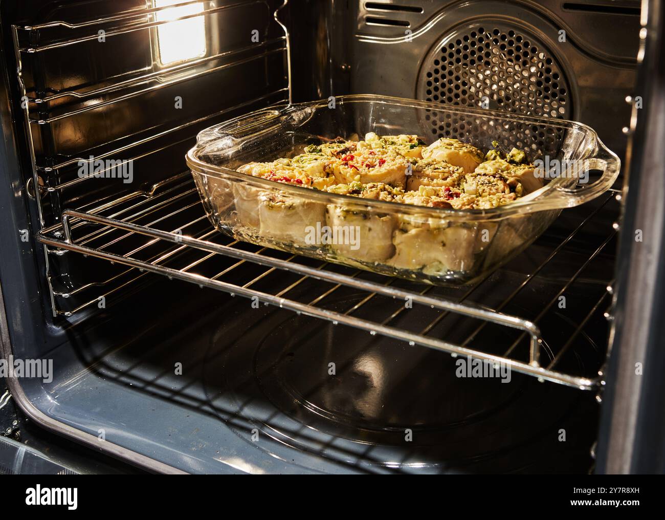 Involtini di verdure freschi cotti in un piatto di vetro all'interno di un forno, seguiti dal risultato finale panini dorati con semi di sesamo. Foto Stock