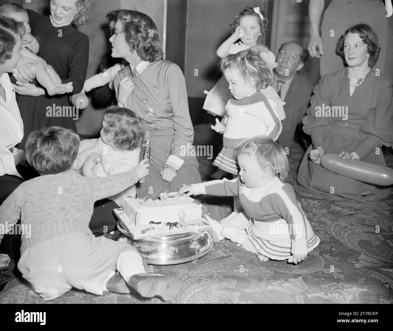 PIZZICARE LA TORTA MENTRE GLI ALTRI NON GUARDANO. Io. 2,54 per celebrare il primo anniversario dello spettacolo "Paint Your Wagon" al Her Majesty's Theatre di Haymarket, Londra, Jack Hylton ha dato una festa ai bambini dei membri del cast e ha presentato a ciascuno dei bambini un carro dipinto giocattolo. N. P. Photo Shows. La gemella di 16 mesi Lynn, figlia della ballerina Veit Bethke, ruba una fetta di torta mentre il resto dell'attenzione della compagnia è concentrata altrove. W/74471 International News Photos. Foto di R. Palmer. Foto Stock