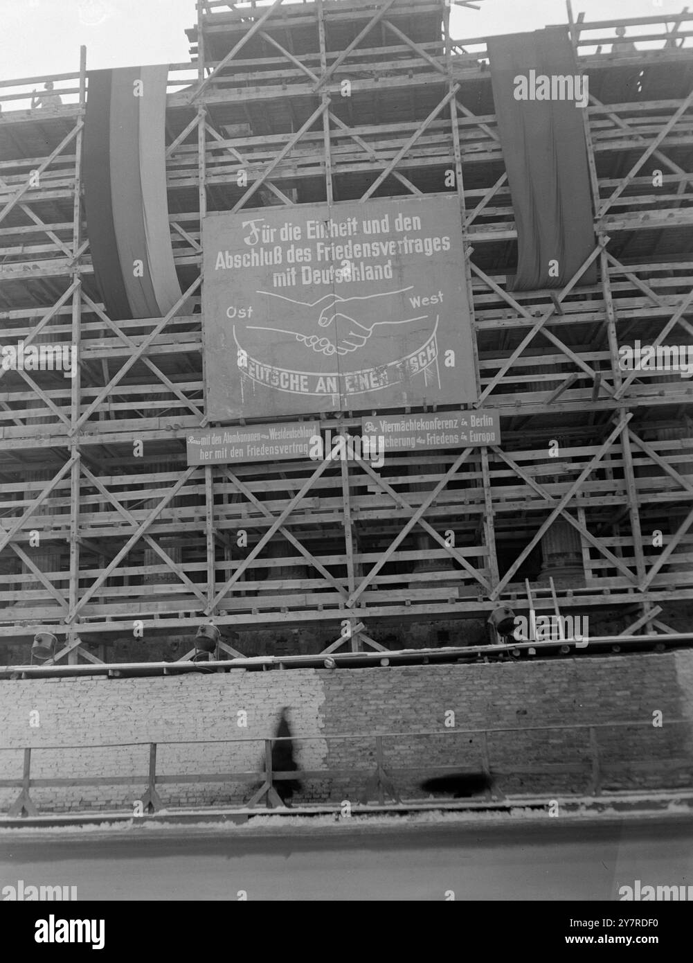 SETTORE ORIENTALE DI BERLINO 1.27.54 fotografo I.N.P. visita il settore orientale di Berlino con il permesso concesso dalle autorità sovietiche per la durata della conferenza. La foto mostra: La costruzione di Stalinallee, il fronte di fantasia che il settore sovietico di Berlino presenta ai visitatori mentre le aree di distruzione in tempo di guerra rimangono intatte. L'esposizione propagandistica ha bandiere russe e tedesche orientali che fiancheggiano un poster che mostra l'accordo est-ovest (mani collegate) e la "unità" tedesca possibile solo se i tedeschi dell'est sono ammessi ai grandi quattro colloqui. Foto INP di Bohnacker. Foto Stock