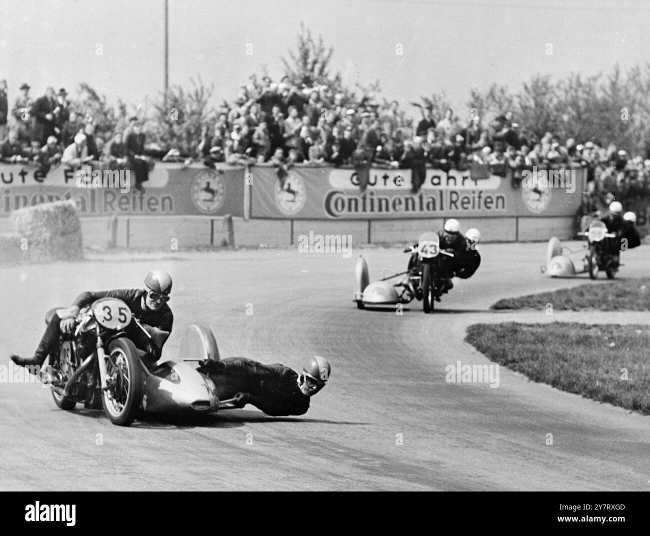 LE GARE MOTOCICLISTICHE TEDESCHE ATTIRANO VISITATORI INTERNAZIONALI Una folla stimata a 100.000 persone che la domenica a Hockenheim, in Germania, hanno sfidato il freddo per assistere a un ingresso internazionale di motociclisti che gareggiano su un percorso di 7.725 chilometri. La foto mostra il britannico Eric Oliver (No. 35) su una Norton, vincitrice dell'evento sidecar 500 c. 13 maggio 1953 Foto Stock